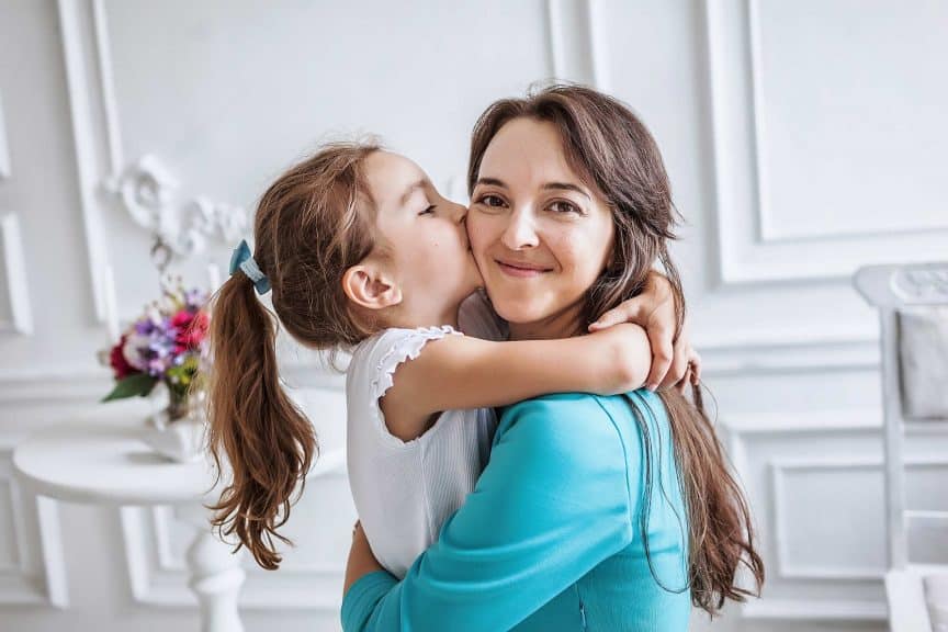 10 year old embracing and kissing her smiling beautiful mother