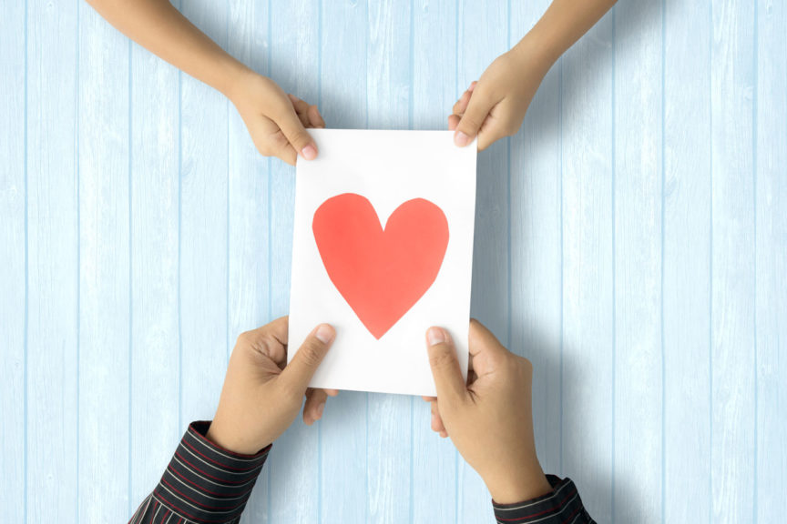 Couple Holding Paper With Heart Shape On Table