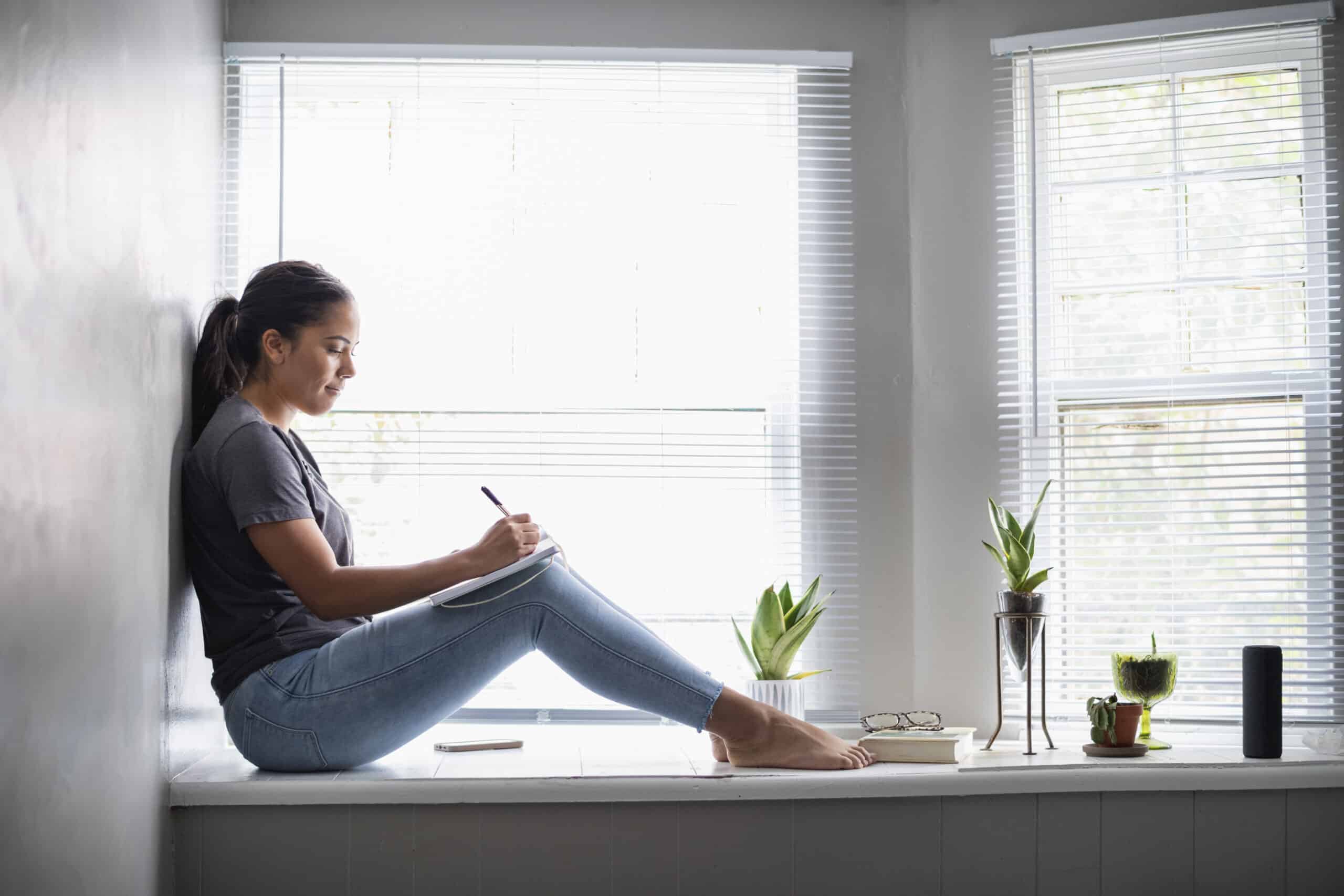 Woman sitting in widow seat writing