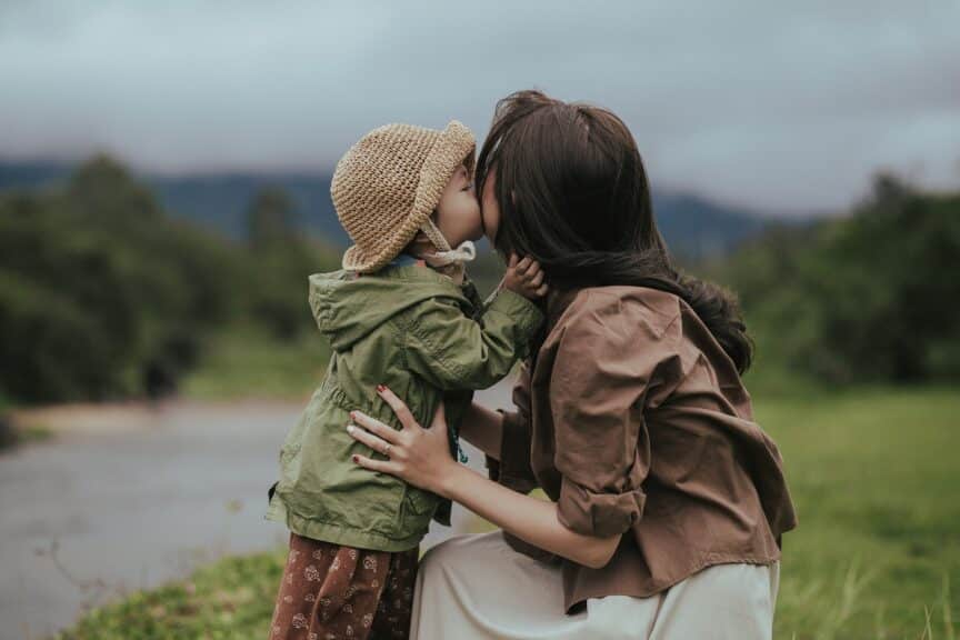 child kissing mother on cheek outside on cloudy day