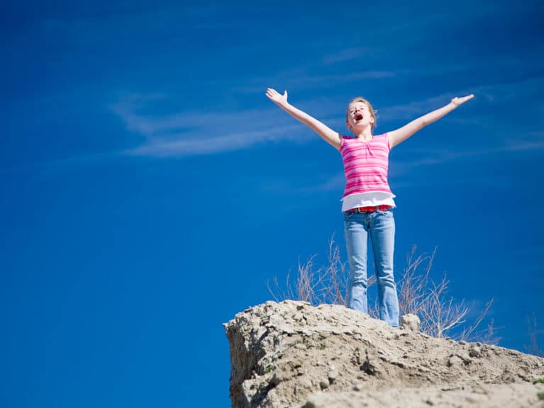 A young girl standing on a cliff with her arms outstretched